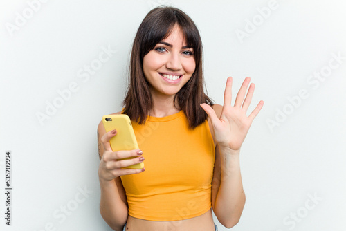 Young caucasian woman using mobile phone isolated on white background smiling cheerful showing number five with fingers.