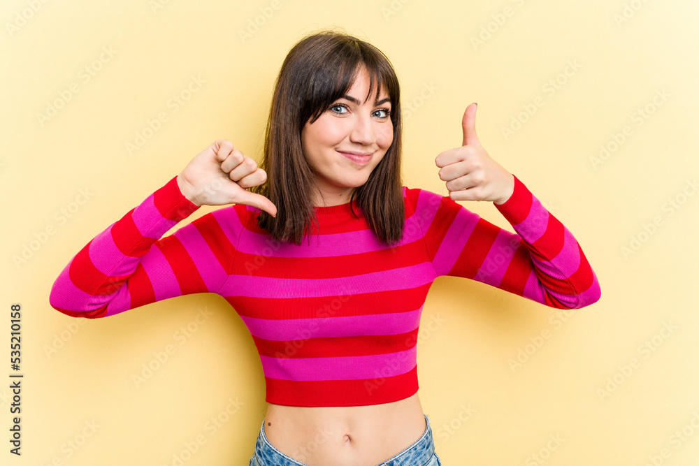Young caucasian woman isolated on yellow background showing thumbs up and thumbs down, difficult choose concept