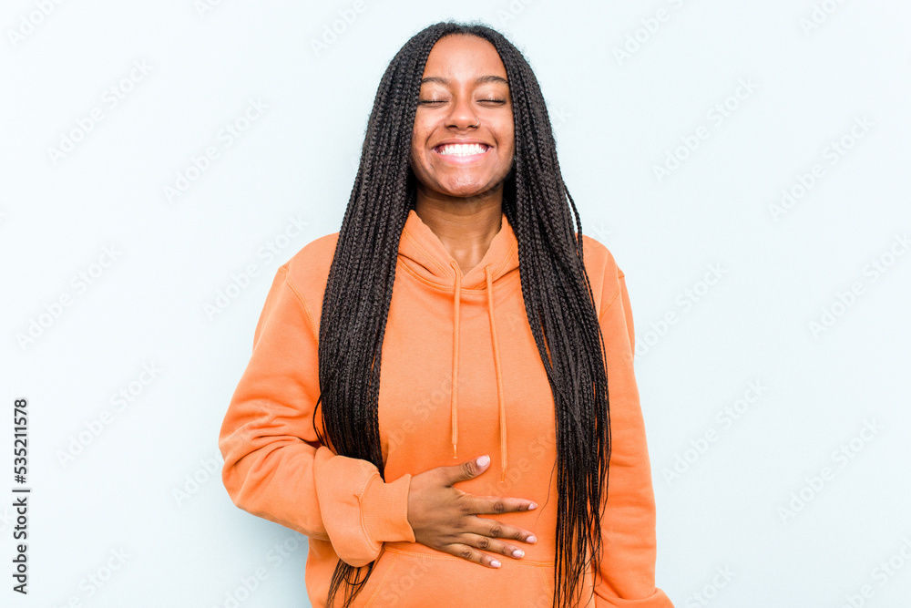 Young African American woman with braids hair isolated on blue background touches tummy, smiles gently, eating and satisfaction concept. Young African American woman with braids hair isolated on blue background touches tummy, smiles gently, eating and satisfaction concept.