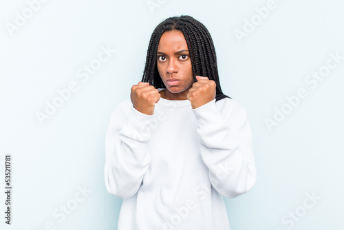 Young African American woman with braids hair isolated on blue background throwing a punch, anger, fighting due to an argument, boxing.