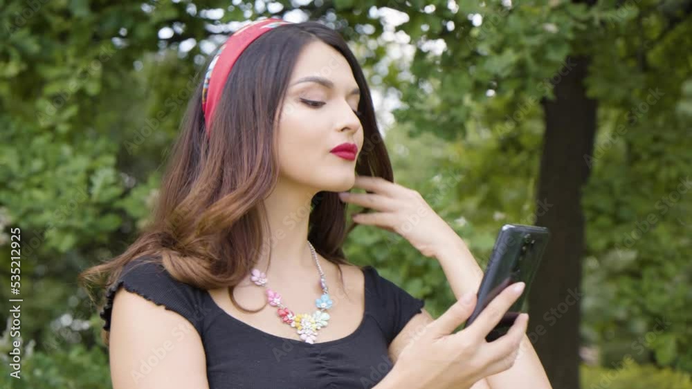 A young beautiful Caucasian woman fixes her hair and uses her smartphone as a mirror A young beautiful Caucasian woman fixes her hair and uses her smartphone as a mirror