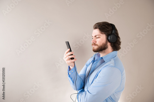 Excited cheerful man wearing blue shirt isolated over gray background, wearing earphones, using mobile phone