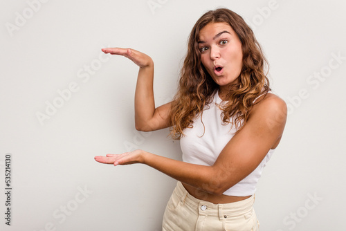Young caucasian woman isolated on blue background shocked and amazed holding a copy space between hands.
