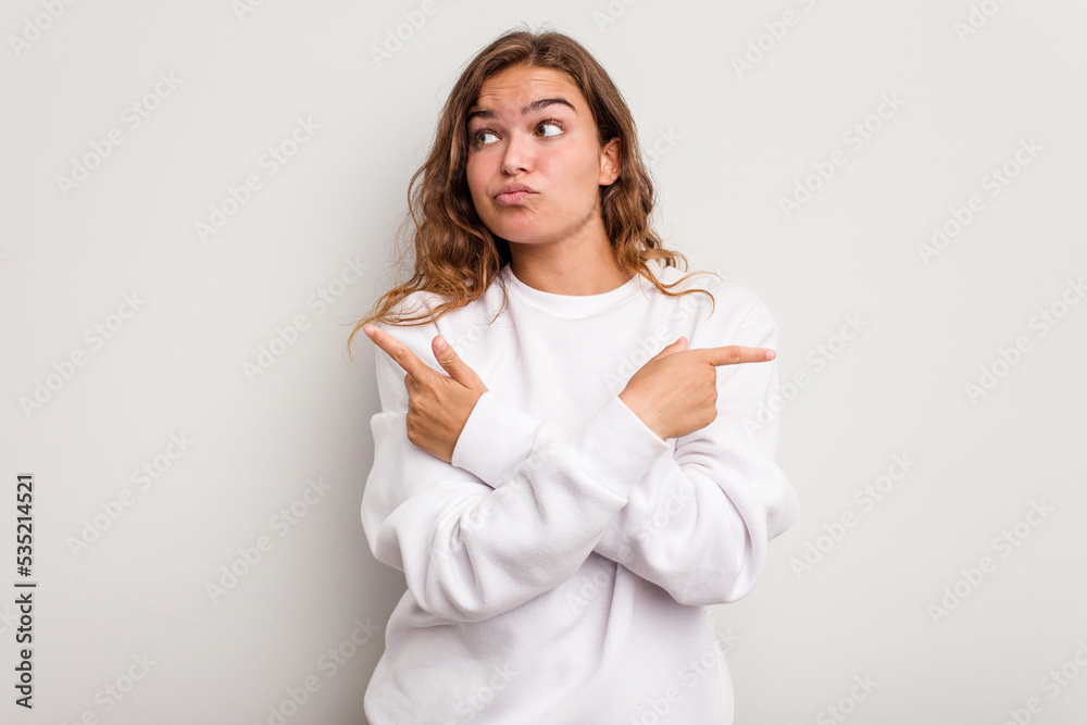 Young caucasian woman isolated on blue background points sideways, is trying to choose between two options. Young caucasian woman isolated on blue background points sideways, is trying to choose between two options.