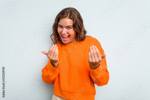Young caucasian woman isolated on blue background pointing with finger at you as if inviting come closer.