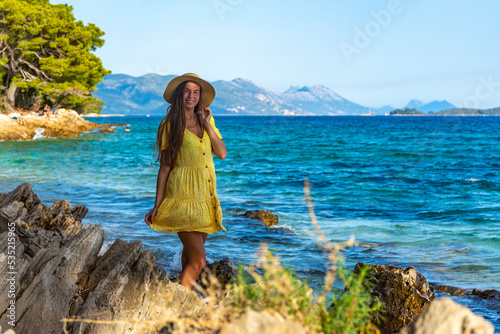 beautiful long-haired girl in a yellow dress enjoys the sunset on a paradise beach in croatia, peljesac peninsula and its paradise bays