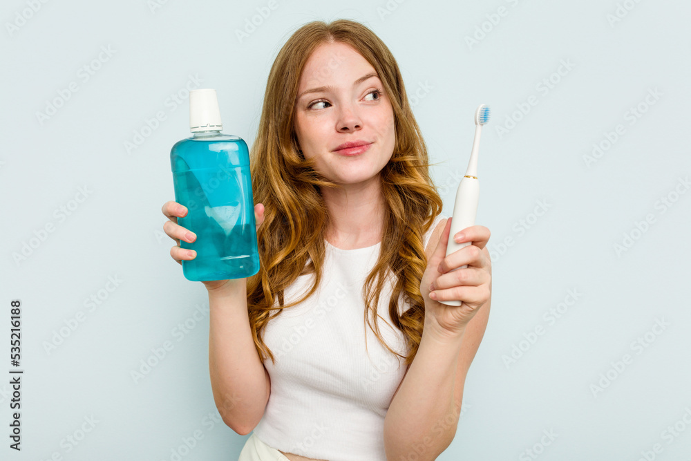 Young caucasian woman holding a mouthwash and toothbrush isolated on blue background Young caucasian woman holding a mouthwash and toothbrush isolated on blue background