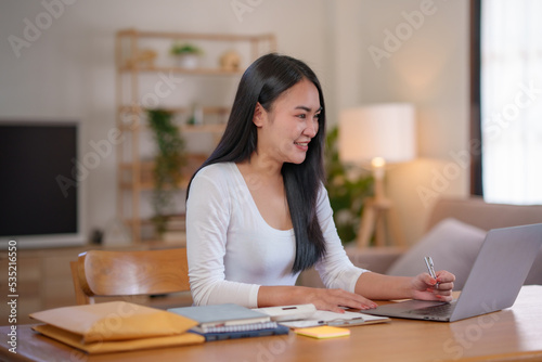 Beautiful Asian woman sitting intently working on a laptop computer at home.