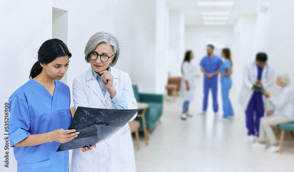 Nurse with female radiologist looking at brain MRI, standing in hospital corridor while working day. Health care institution