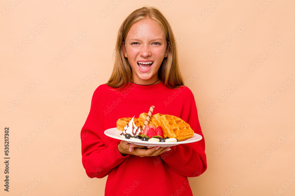 Little caucasian girl holding a waffles isolated on beige background screaming very angry and aggressive.