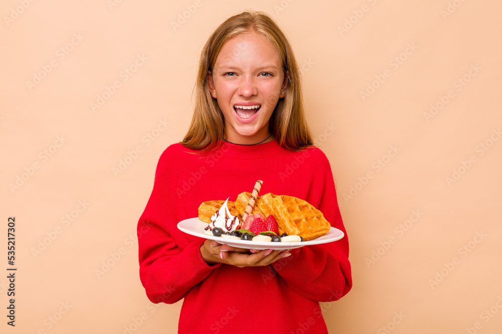 Little caucasian girl holding a waffles isolated on beige background screaming very angry and aggressive. Little caucasian girl holding a waffles isolated on beige background screaming very angry and aggressive.
