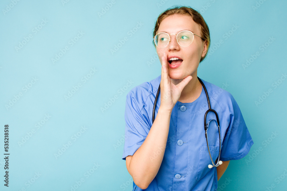 Young nurse caucasian woman isolated on blue background is saying a secret hot braking news and looking aside
