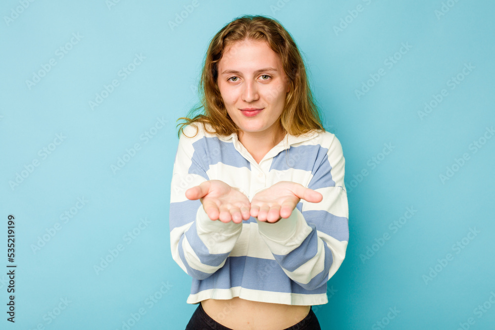Young caucasian woman isolated on blue background holding something with palms, offering to camera. Young caucasian woman isolated on blue background holding something with palms, offering to camera.