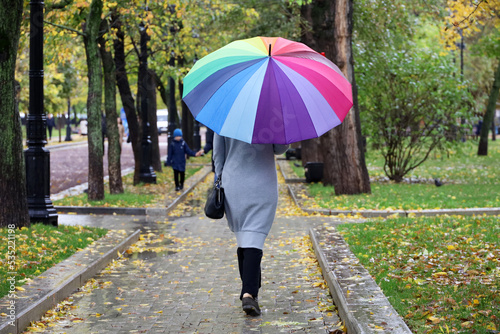 Rain in city, slim woman with colorful umbrella wearing grey coat walking down the street. Rainy weather in autumn park