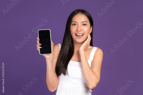 Beautiful Asian brunette woman cute girl in white tank top ,Excited surprised girl showing smart phone with blank screen , black screen isolated purple background , Mock Up Image