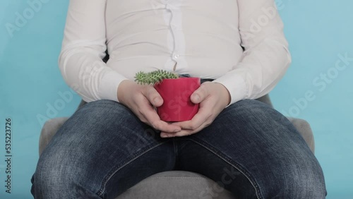 An office worker in a white shirt sits on a chair and holds a red cactus pot in his hands. The concept of chronic male diseases with a sedentary lifestyle, close-up