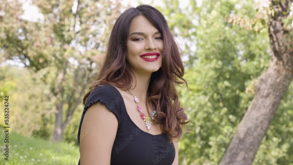 A young beautiful Caucasian woman smiles at the camera in a park on a sunny day A young beautiful Caucasian woman smiles at the camera in a park on a sunny day