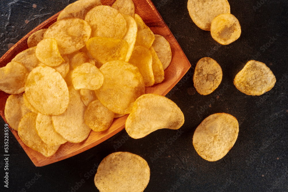 Potato chips or crisps, a salty snack in a bowl, a flat lay shot on a dark stone background