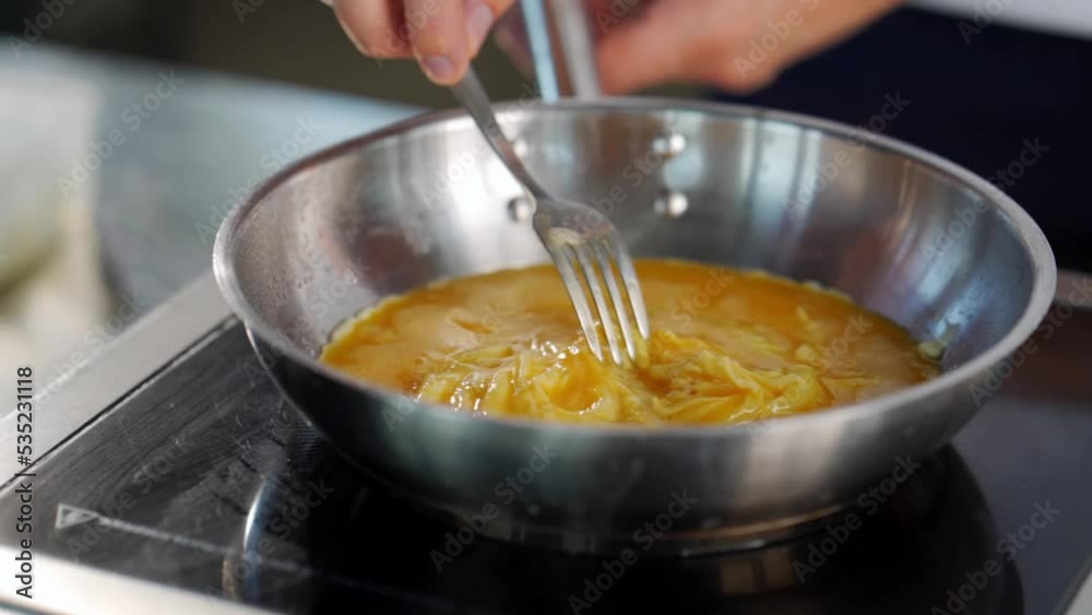 a chef cooks an omelette in a metal pan in a loft-style kitchen a chef cooks an omelette in a metal pan in a loft-style kitchen