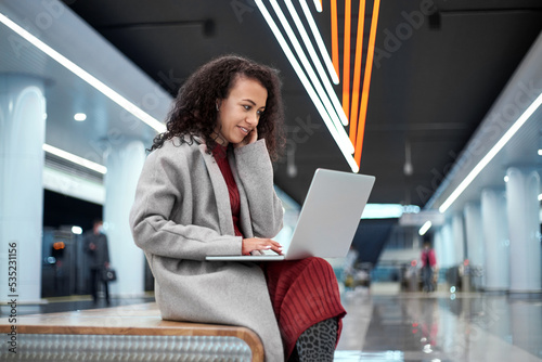 female blogger uses a laptop while sitting on a bench in the subway.