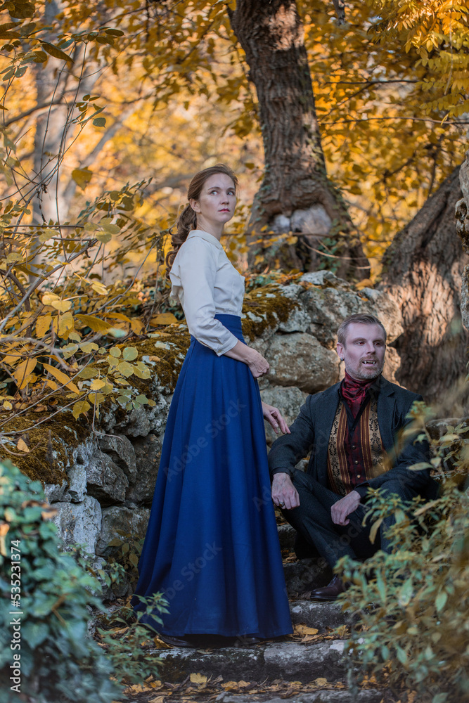 Vampire man wearing victorian suit with vampire woman in the autumn forest. Vintage medieval concept style. Vampire man wearing victorian suit with vampire woman in the autumn forest. Vintage medieval concept style.