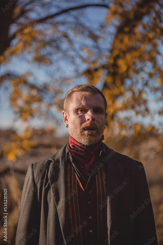 Vampire man wearing victorian suit in the autumn forest. Vintage medieval concept style. Vampire man wearing victorian suit in the autumn forest. Vintage medieval concept style.