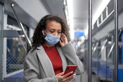 young woman in a protective mask reading a text message in a subway car.