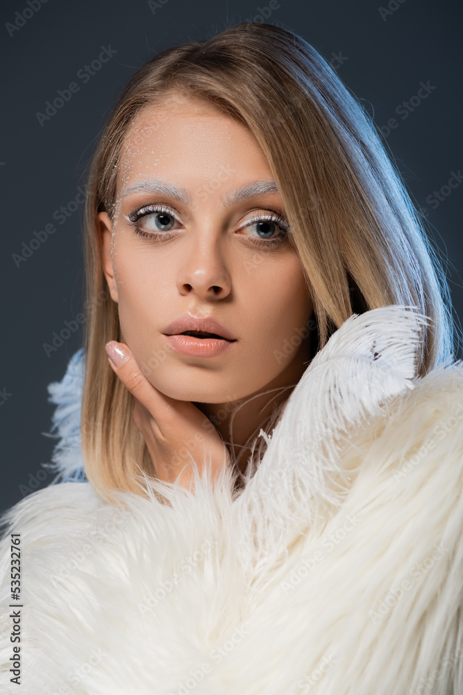 pretty young woman in winter faux fur jacket looking away isolated on blue. pretty young woman in winter faux fur jacket looking away isolated on blue.