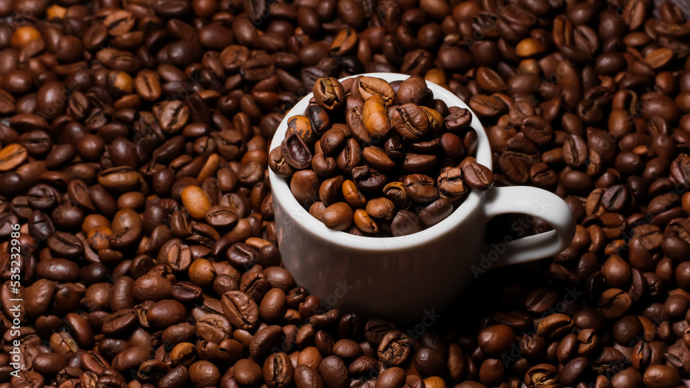 Espresso cup filled with coffee beans surrounded by a large number of coffee beans on a dark background close-up.