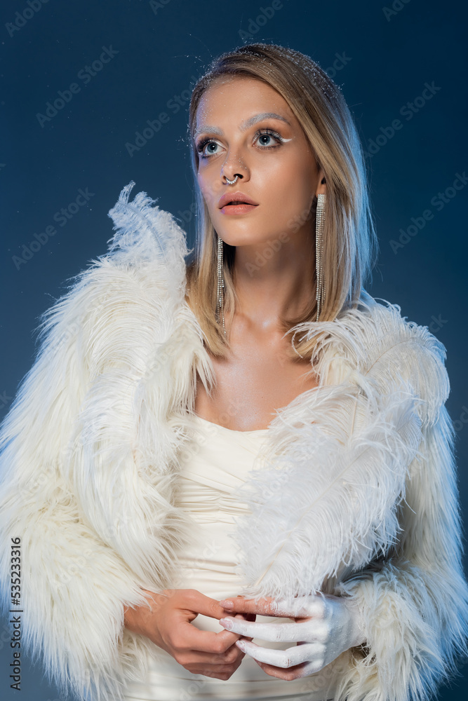 young pierced woman with snow on hair and winter faux fur jacket posing on dark blue. young pierced woman with snow on hair and winter faux fur jacket posing on dark blue.