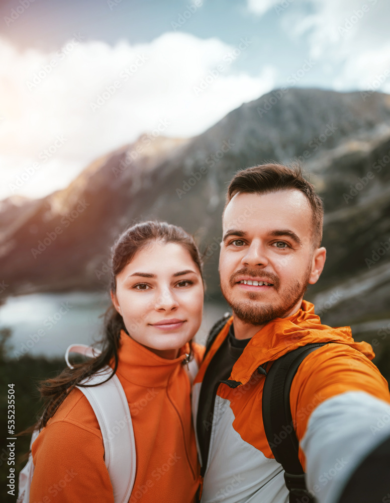 The young couple smiles and looks at the camera with a beautiful mountain and lake background. Family outdoor sports activity in the Tatra Mountains and Morskie Oko
