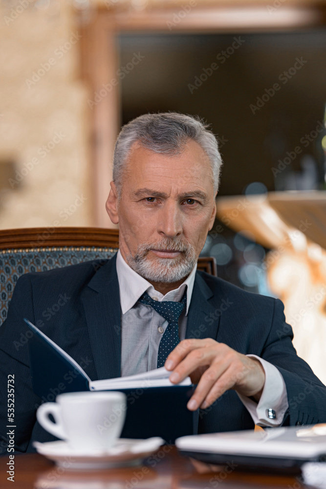 Businessman looking through his diary and drinking coffee while sitting in luxury hotel room Businessman looking through his diary and drinking coffee while sitting in luxury hotel room