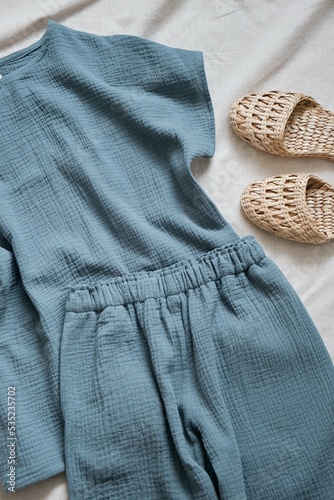 Muslin pajamas made of a blouse and trousers in a beautiful blue color. Nearby are comfortable and stylish home slippers made of natural tropical rattan. High quality photo