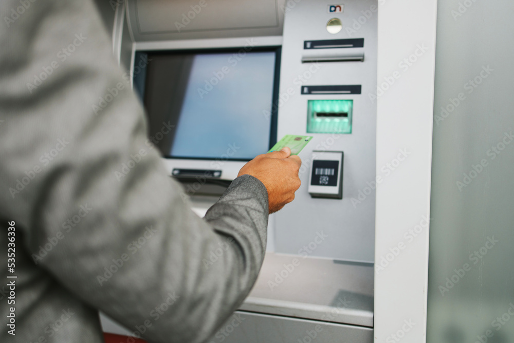 Handsome middle age businessman with eyeglasses standing on city street and using ATM machine to withdraw money from credit or debit card. Hand close up. Handsome middle age businessman with eyeglasses standing on city street and using ATM machine to withdraw money from credit or debit card. Hand close up.