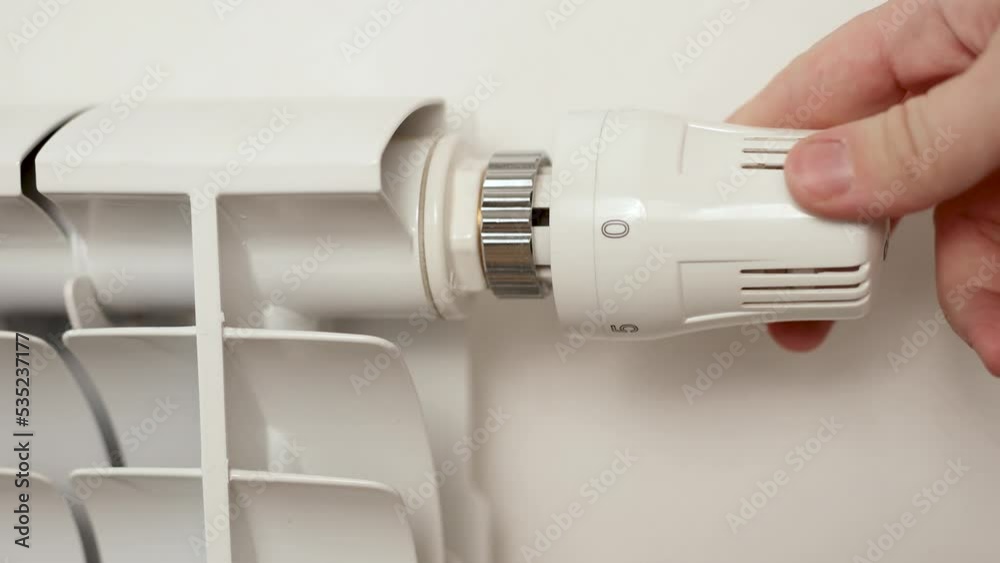 White heating radiator hanging on white wall, close up view. Person turns off radiator. Central heating system. Heating is getting more expensive, save money. Energy crisis. White heating radiator hanging on white wall, close up view. Person turns off radiator. Central heating system. Heating is getting more expensive, save money. Energy crisis.