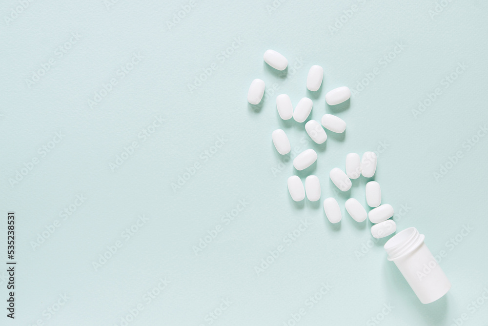 white pills and a plastic container on a blue background. Medical theme. white pills and a plastic container on a blue background. Medical theme.