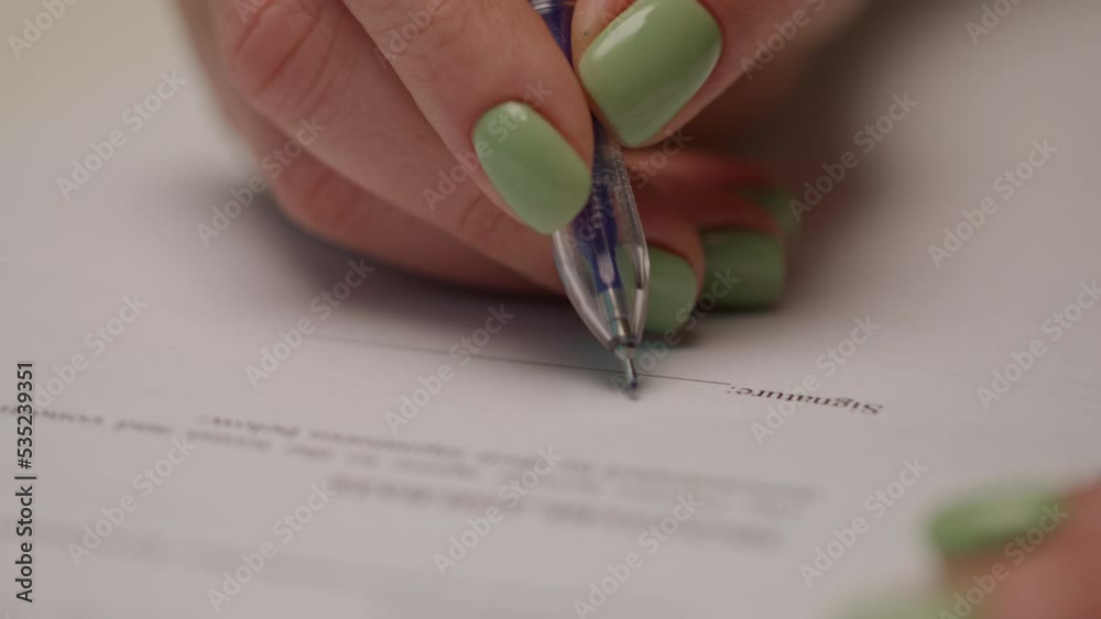 Female hand signing paper document with pen. Handwriting signature on document.