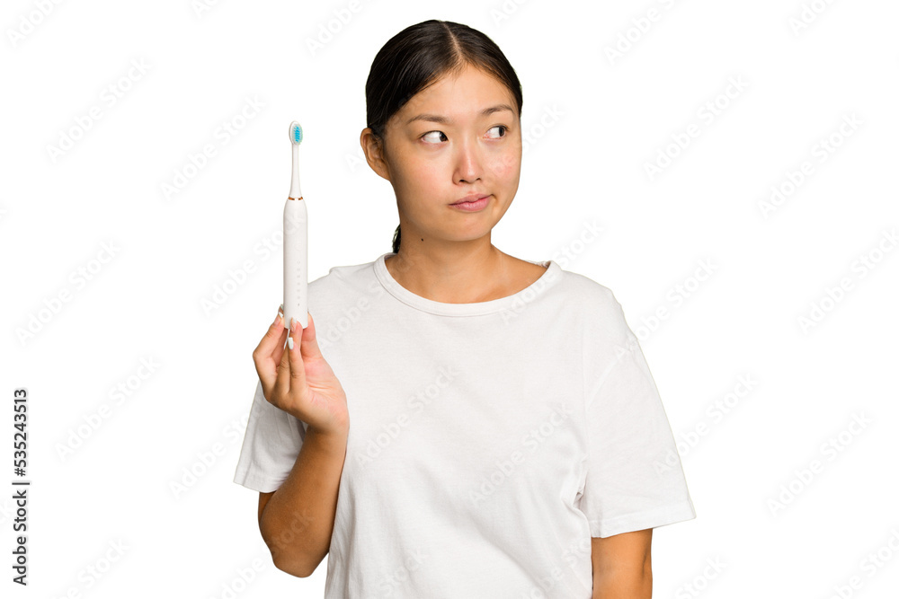 Young Asian woman holding an electric toothbrush isolated on green chroma background confused, feels doubtful and unsure. Young Asian woman holding an electric toothbrush isolated on green chroma background confused, feels doubtful and unsure.