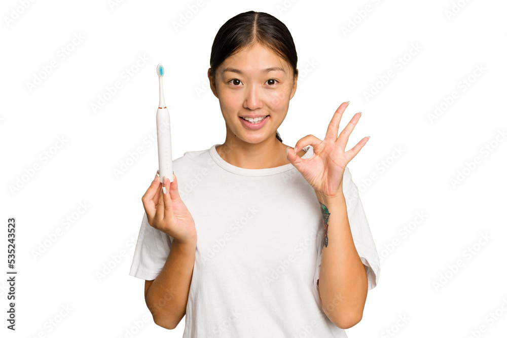 Young Asian woman holding an electric toothbrush isolated on green chroma background cheerful and confident showing ok gesture. Young Asian woman holding an electric toothbrush isolated on green chroma background cheerful and confident showing ok gesture.