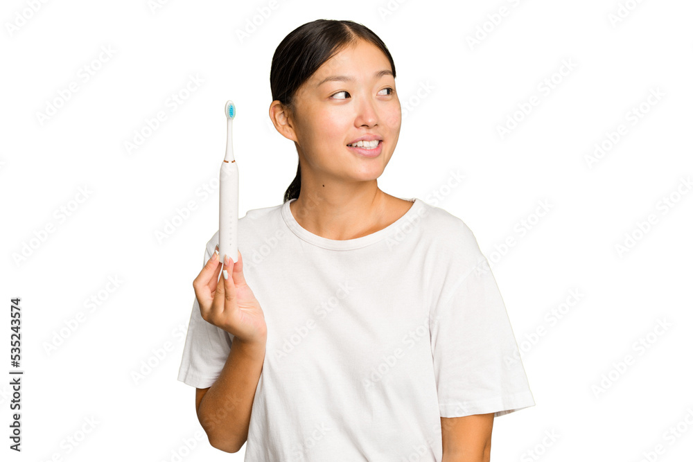 Young Asian woman holding an electric toothbrush isolated on green chroma background looks aside smiling, cheerful and pleasant. Young Asian woman holding an electric toothbrush isolated on green chroma background looks aside smiling, cheerful and pleasant.
