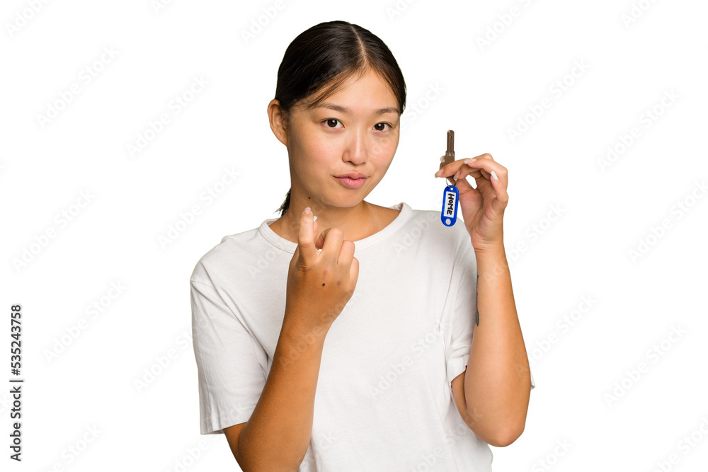 Young asian woman holding home keys isolated on green chroma background pointing with finger at you as if inviting come closer. Young asian woman holding home keys isolated on green chroma background pointing with finger at you as if inviting come closer.
