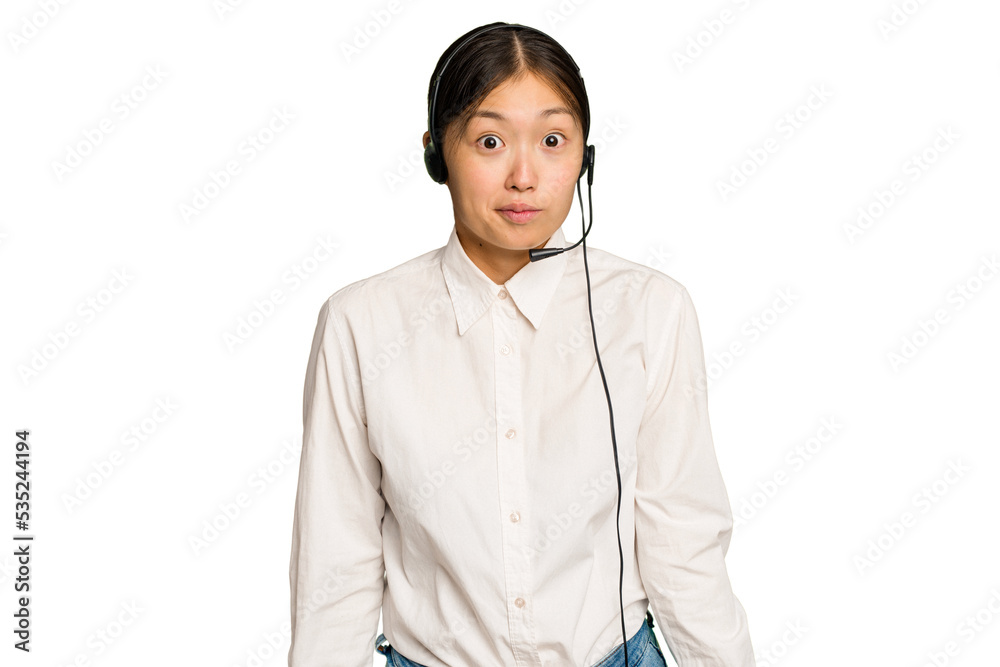 Telemarketer asian woman working with a headset isolated on green chroma background shrugs shoulders and open eyes confused. Telemarketer asian woman working with a headset isolated on green chroma background shrugs shoulders and open eyes confused.
