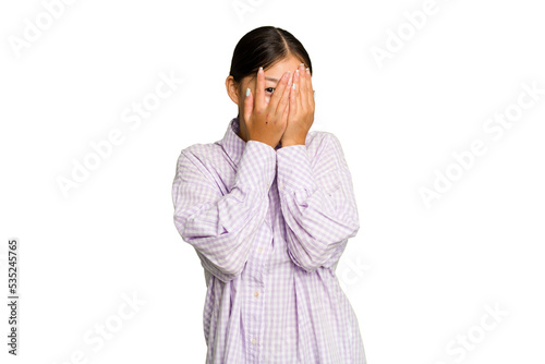 Young Asian woman isolated on green chroma background blink at the camera through fingers, embarrassed covering face.