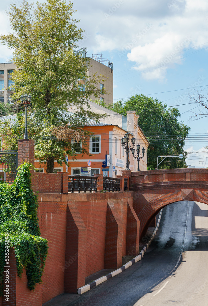 Picturesque red stone bridge overhangs across the road. Bridge was  designed by Voronezh architect Ivan Blitsyn in 1826. Voronezh, Russia - July 30, 2022