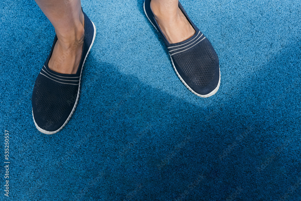 Slip-ons of dark blue color on female legs. Bright blue rubber running track.