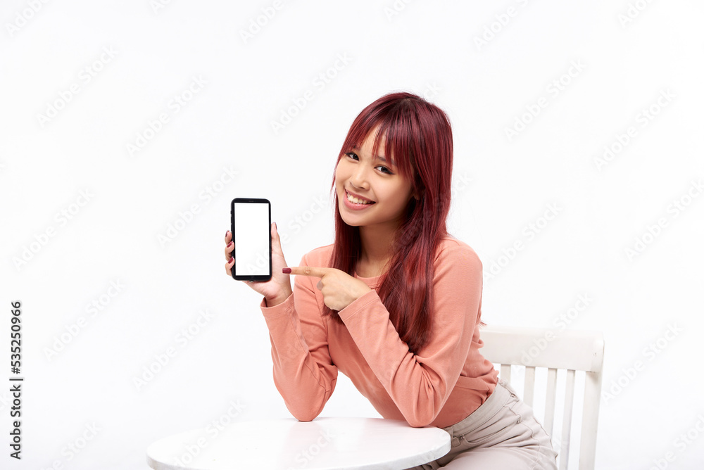 Portrait of attractive Asian young woman smiling and spointing at smartphone with empty screen. Demonstrate an app or online shopping store. Isolated in studio background. Portrait of attractive Asian young woman smiling and spointing at smartphone with empty screen. Demonstrate an app or online shopping store. Isolated in studio background.