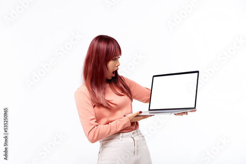 Amazed beautiful Asian teen showing you a blank of laptop screen standing isolated in white background. Concept of advertising, emotions, shopping, technology. Copy space, Blank photo