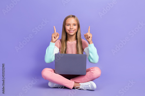 Full length photo of cheerful girl sit floor hand show empty space recommend offer device shop sale isolated on purple color background © deagreez