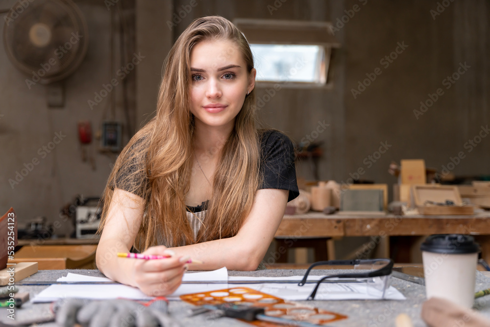 Fototapeta premium Portrait of a female carpenter drawing on paper for designing and building furniture in a furniture factory. with modern tools