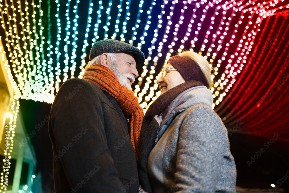 Elderly couple in romantic embrace under the colorful Christmas lights
